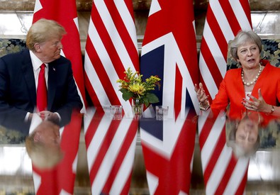 Donald Trump e Theresa May seduti dietro un tavolo di specchio su cui si riflettono le bandiere americana e inglese.