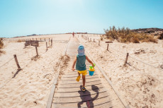 Un bambino, secchiello in mano, corre sulla spiaggia verso il mare.