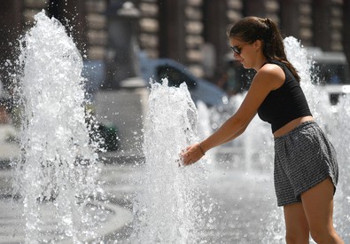 Una ragazza si rinfresca con l'acqua di una fontana pubblica.