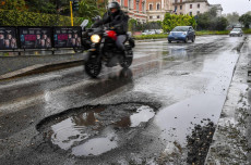 Un motociclista passa vicino una buca sull'asfalto bagnato