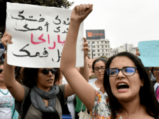 Donne protestano con il braccio alzato e u cartello con scritta in arabo.