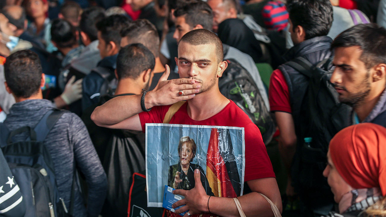 Un immigrato siriano in Germania con la foto della Merkel saluta inviando un bacio