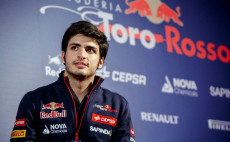 Primo piano di Carlos Sainz, alle spalle il tabellone pubblicitario con Toro Rosso