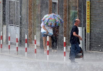 Sotto il temporale una persona cammina con l'ombrella e un'altra a capo scoperto