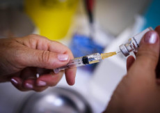 Vaccini: la mano di una dottoressa prelevando il vaccino dalla fiala con una siringa.