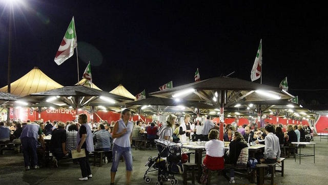 Persone sedute ai tavoli della Festa dell'Unità di sera.