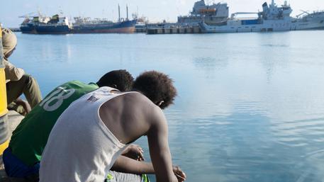 Due migranti seduti sul bordo del porto.
