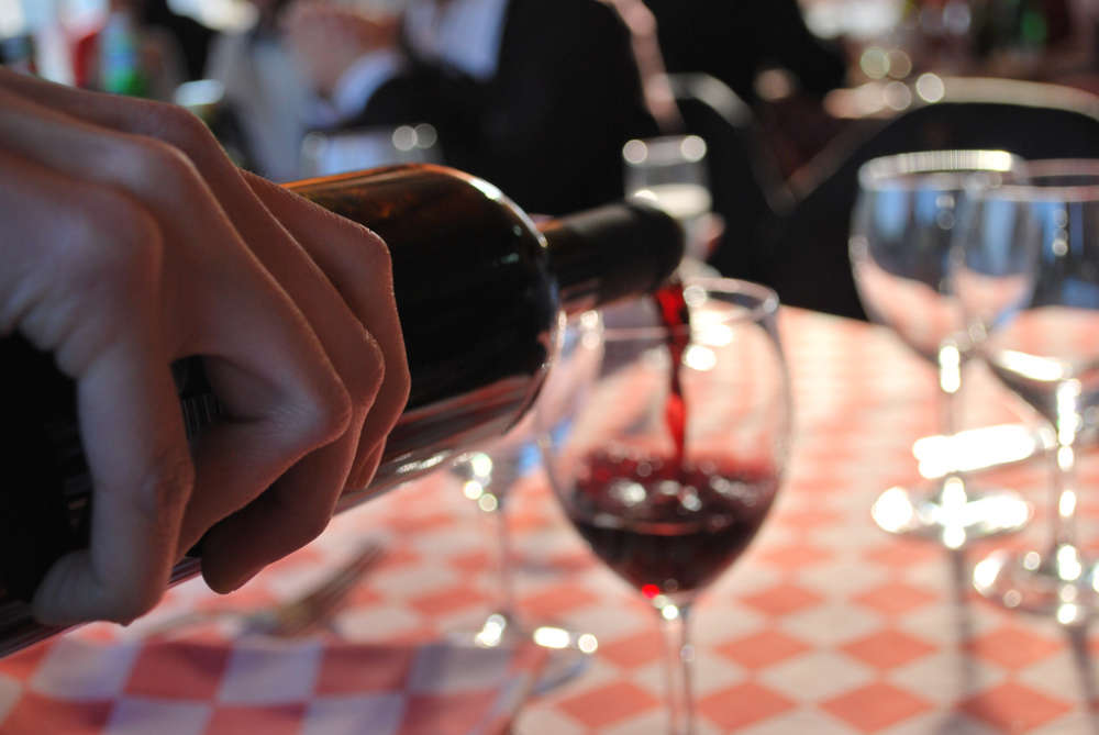 Una bottiglia di vino rosso tenuta per mano, versa il vino in un bicchiere