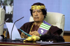Gheddafi seduto al suo tavolo di lavoro, con vestito delle sua tribù.