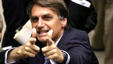 Primo piano di Bolsonaro con le mano in atto di sparare. Brasile