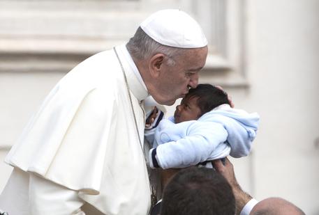 Papa Francesco durante una audizione generale a Piazza San Pietro bacia un bambino.