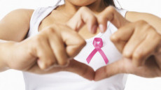 Una donna forma con le dita il simbolo del cuore e dentro quello del tumore al seno.