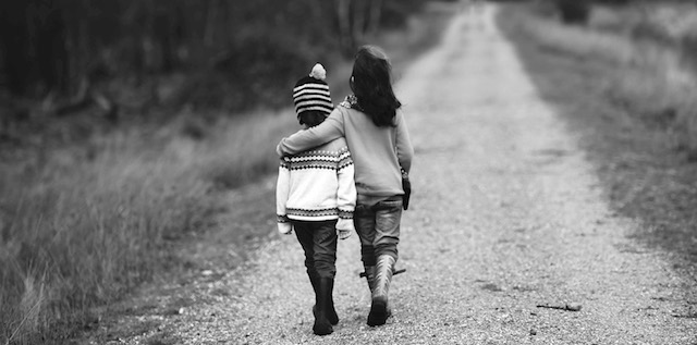 Un bambino abbraccia l'altro camminando su una strada sterrata.