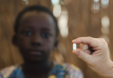 Un bambino africano, in primo piano una mano con una pillola.
