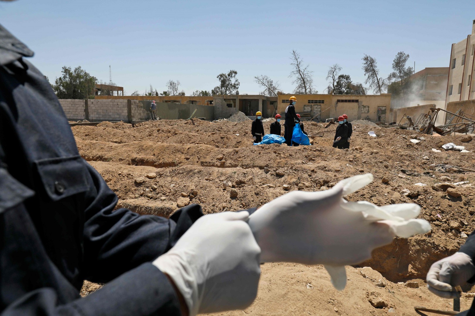 Un funzionario indossa i guanti di lattice bianchi sullo sfondo il campo con le fosse comuni. Isis