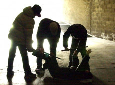 Foto in penombra, tre ragazzi stanno malmenando un loro coetaneo steso a terra.