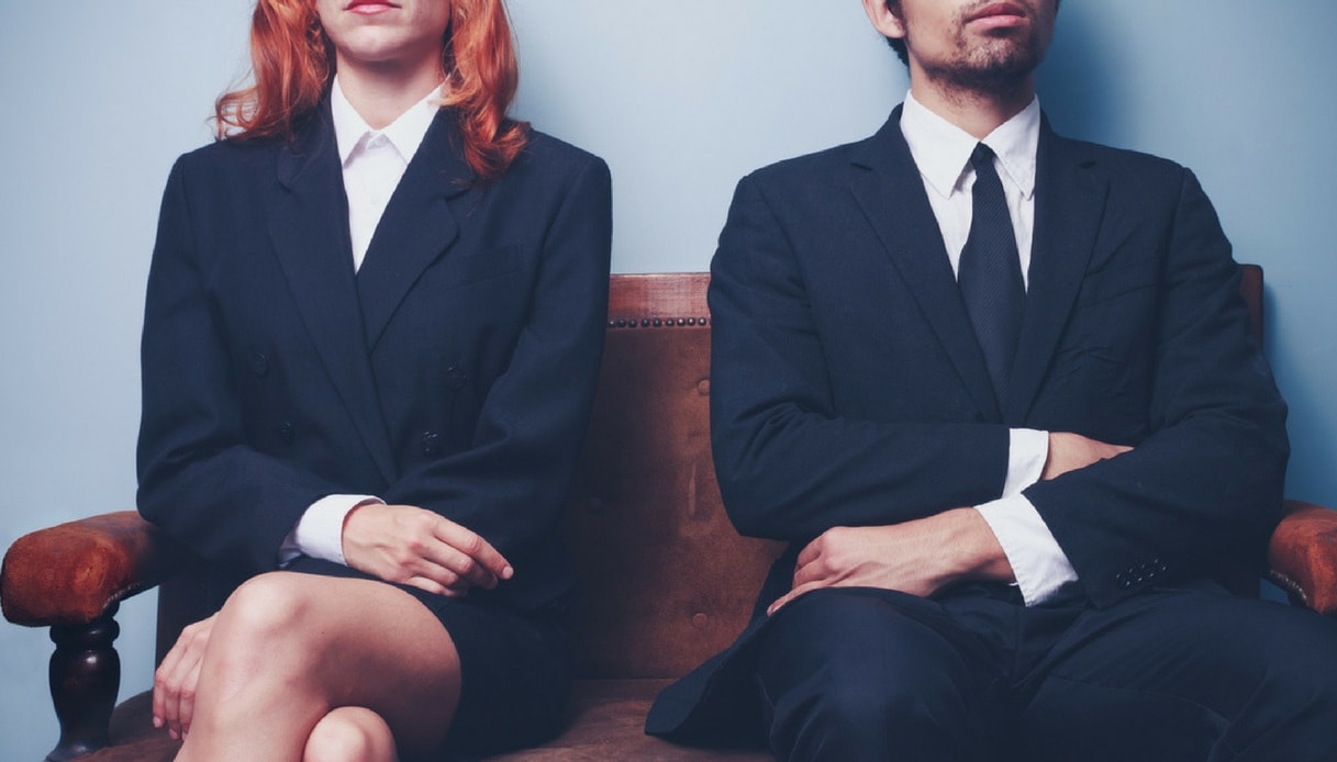Un ragazzo e una ragazzi vestiti di nero, seduti in attesa di di un colloquio di lavoro. Parità