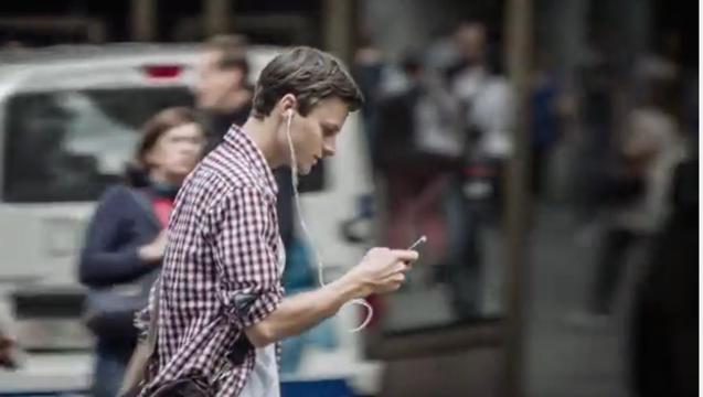 Un ragazzo attraversa la strada guardando il cellulare. Telefonini