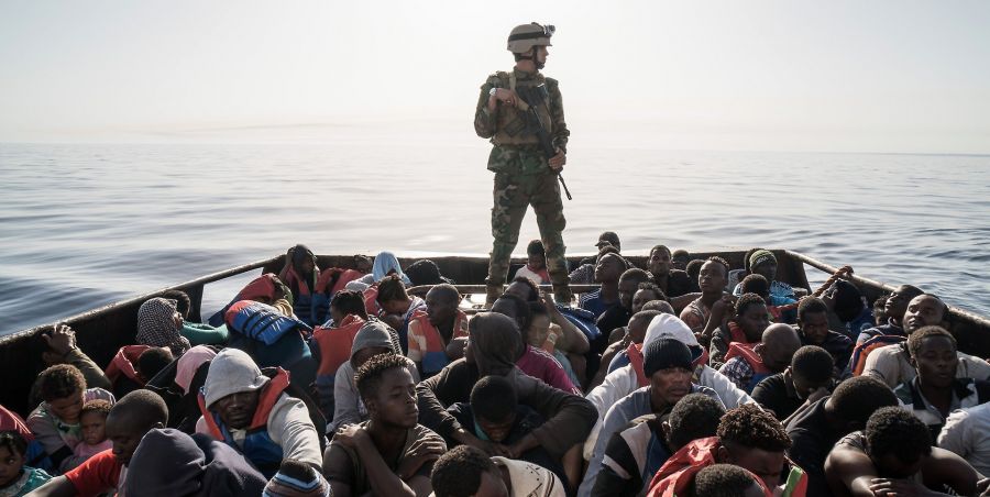 Migranti a bordo di un'imbarcazione controllati da un soldato armato.