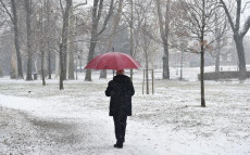 Un uomo camminando in un parco sotto i primi fiocchi di neve.