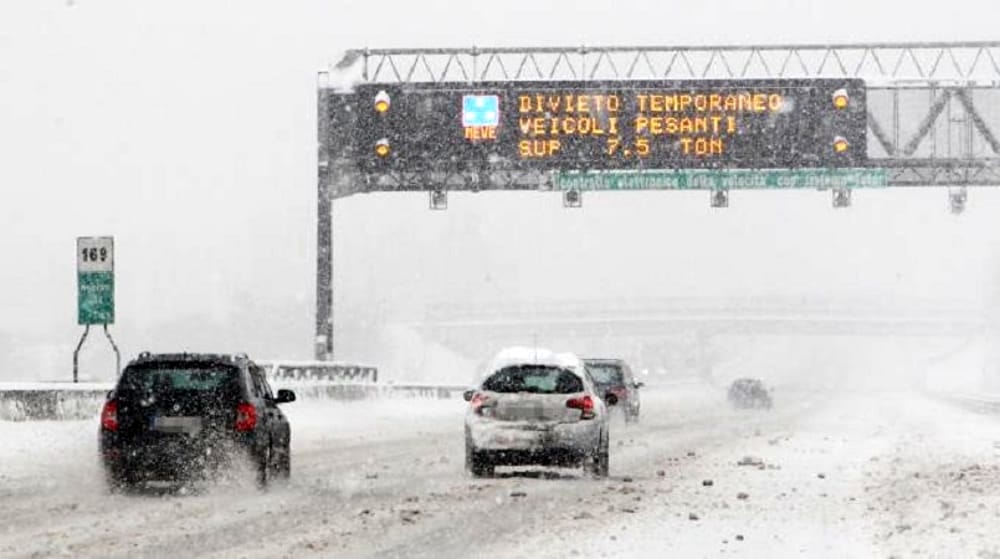 Macchine in autostrada innevata. La segnaletica indica il pericolo di neve e ghiaccio.