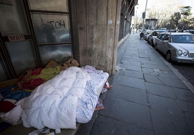 Un senzatetto per strada si difende dal freddo con una coperta.