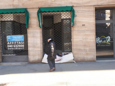 Senzatetto dorme all'entrata di un negozio, un passante osserva la scena.. Trieste