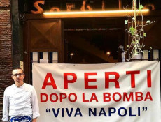 Sorbillo di fronte alla sua pizzeria con il manifesto "Aperto dopo la bomba"
