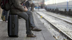 Giovane seduto sulla propria valigia in attesa del treno. Emigrazione