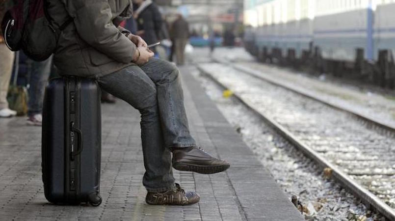 Giovane seduto sulla propria valigia in attesa del treno. Emigrazione