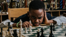Tanitoluwa Adewumi davanti al tavolo di scacchi.