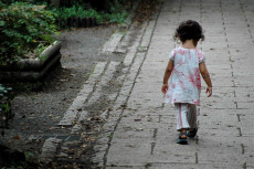 Una bambina sola camminando ai bordi di un'aiuola.