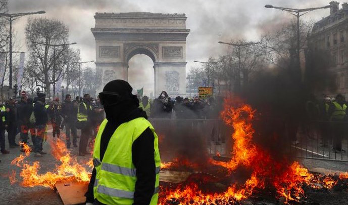 " gilet gialli devastano Parigi, sullo sfondo l'Arco di Trionfo.