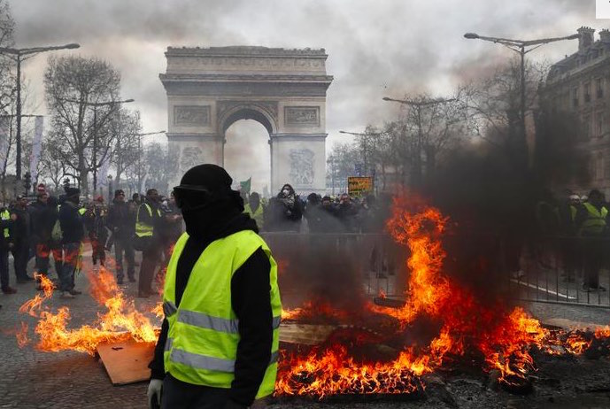 " gilet gialli devastano Parigi, sullo sfondo l'Arco di Trionfo.