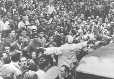Papa Pio XII si rivolge alla folla a braccia aperte.
