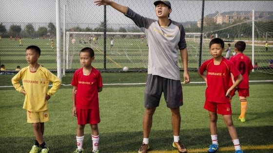 Cina, l'allenatore dà istruzioni ai bambini che lo circondano.