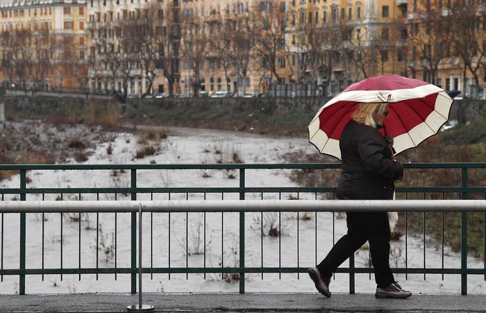 Una donna fotografata sotto la pioggia mentre attraversa un ponte in città.