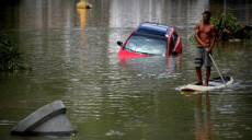 Rio: Dopo le piogge torrenziali un uomo in surf vicino ad un'auto semi sommersa.