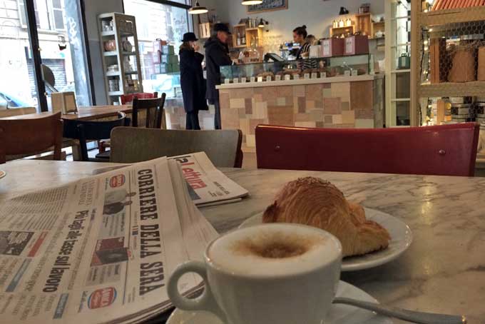 Colazione con cappuccino, brioche e giornale a Milano.