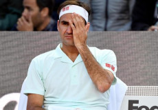 Federer seduto sulla seggiola ai bordi del campo da tennis con una mano sul viso.