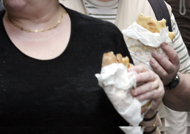 Persona obesa con un cartoccio di patatine fritte in mano.