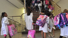 Bambini in grembiulino bianco all'entrata di una scuola.