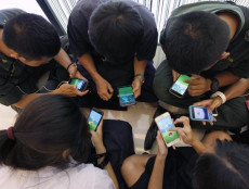 Ragazzi seduti per terra giocano a 'Pokemon Go' con i loro smartphones.