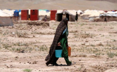 Una donna afghana con due secchi d'acqua in mano, in un campo profughi.