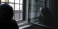 Un ragazzo di fronte ad una finestra e inferriata con felpa incappucciato