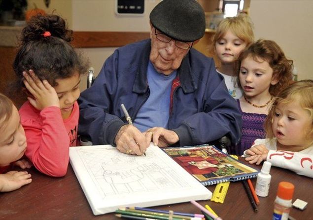 Un anziano esegue dei disegni per dei bambini che gli stanno intorno.