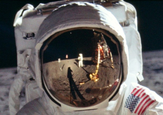 Sulla visiera del casco di un astronauta si specchiano la capsula e gli altri dell'equipaggio.