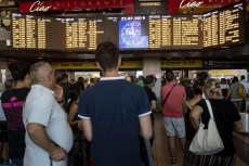 Persone di fronte al tabellone degli arrivi e partenze consultando i ritardi e cancellazioni dei treni alla stazione Termini. Roma