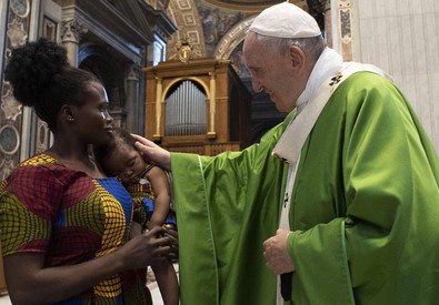 Papa Francesco accarezza un bambino figlio di migranti durante la Messa.