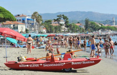 Folla di turisti sulle spiagge della Liguria, pattino rosso di salvataggio in primo piano.